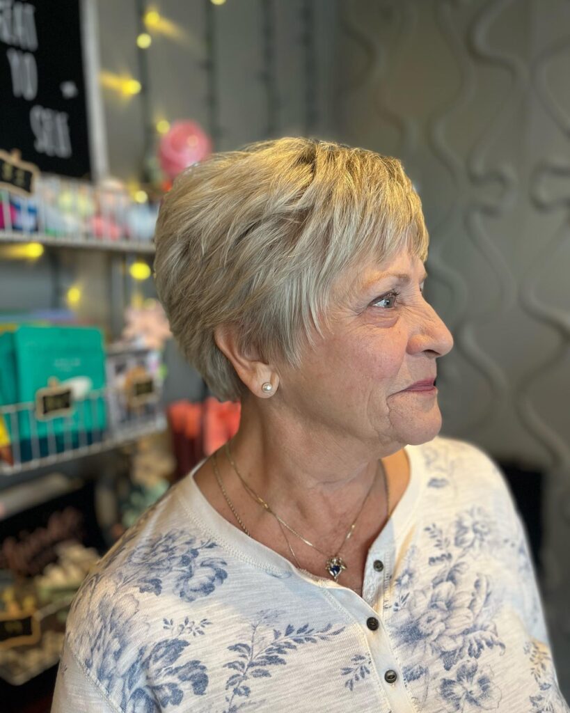 A woman with a soft wispy champagne blonde pixie cut smiling in a side profile.