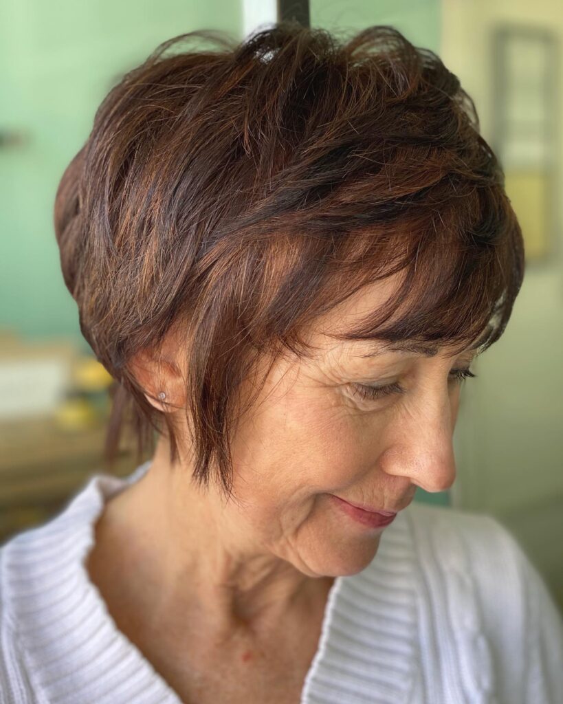 A woman with a short layered auburn wedge haircut and a feathered fringe looking downward.