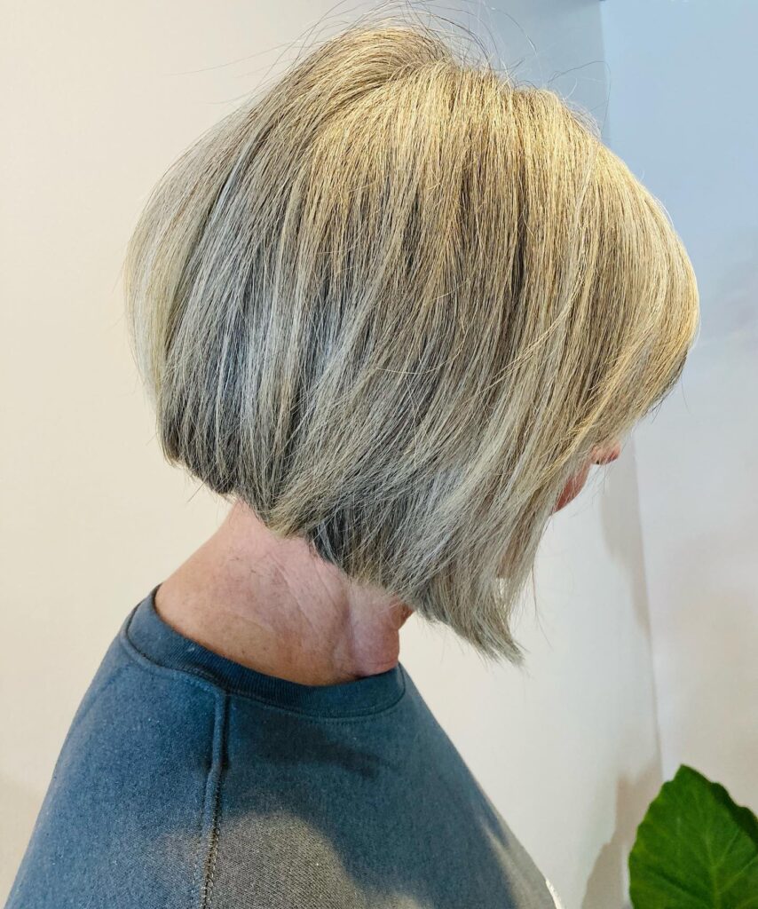 A woman with a stacked ash blonde bob shown from the side to highlight the angled cut and volume in the back.