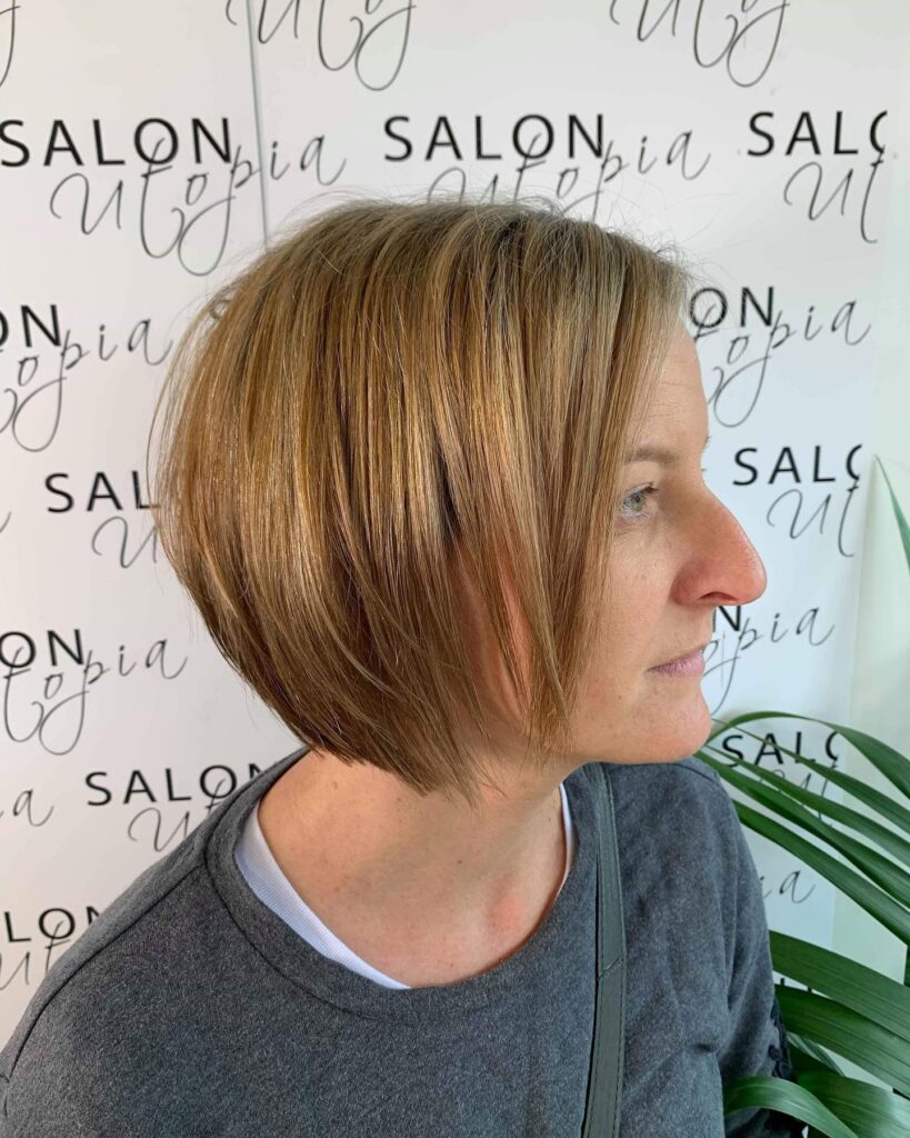 A woman with a sleek and precisely angled caramel blonde A line bob is shown from a profile perspective.