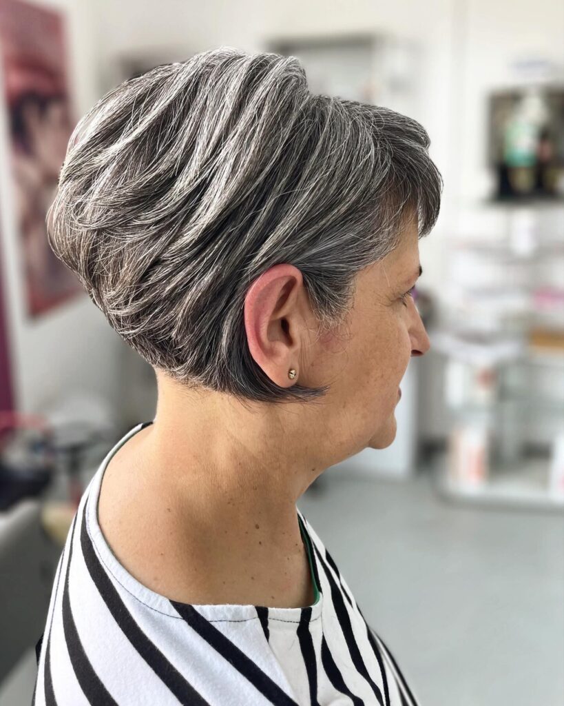 A side profile of a woman with a stacked silver and grey wedge haircut featuring voluminous layers and a tapered nape.