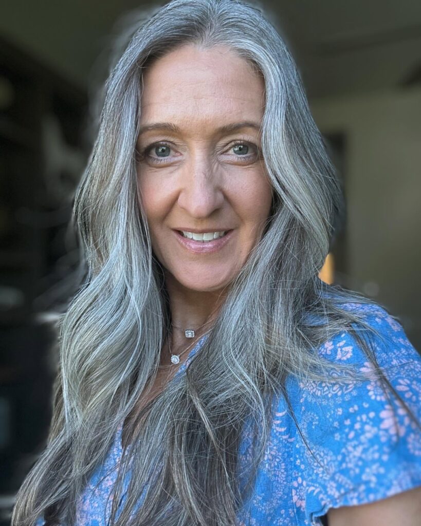 A woman with long wavy silver hair featuring soft face framing layers and a natural grey color blend.