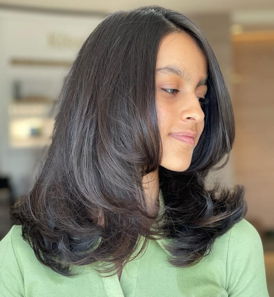 Medium length layered brunette hairstyle with softly flipped ends.