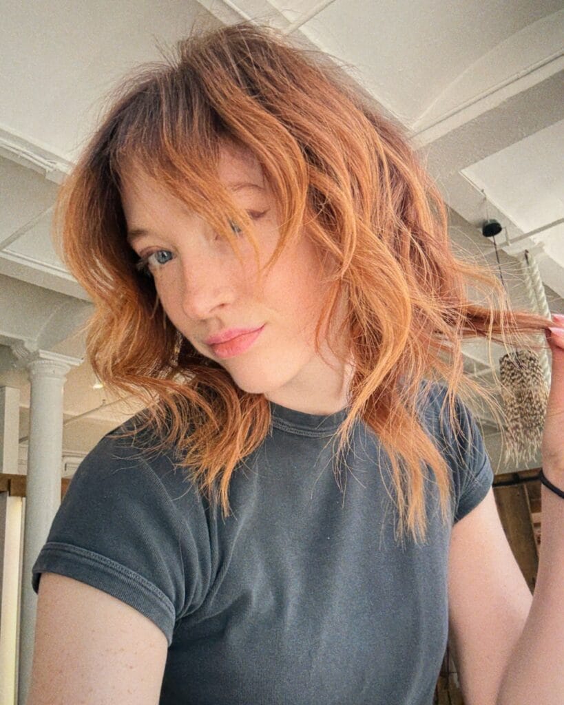 Medium length copper wavy hairstyle with light layers and a soft wispy fringe.