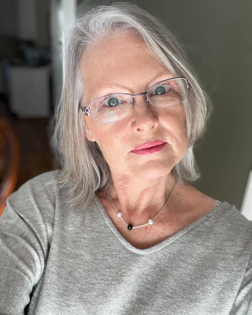 A woman with shoulder length straight gray hair styled with a center part and smooth finish.