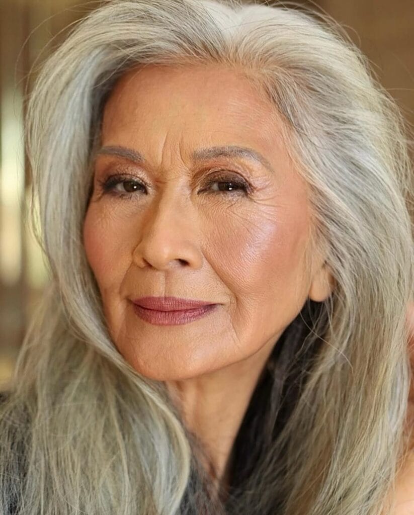 A woman with long silver hair styled in layered waves with soft volume and lift at the crown.