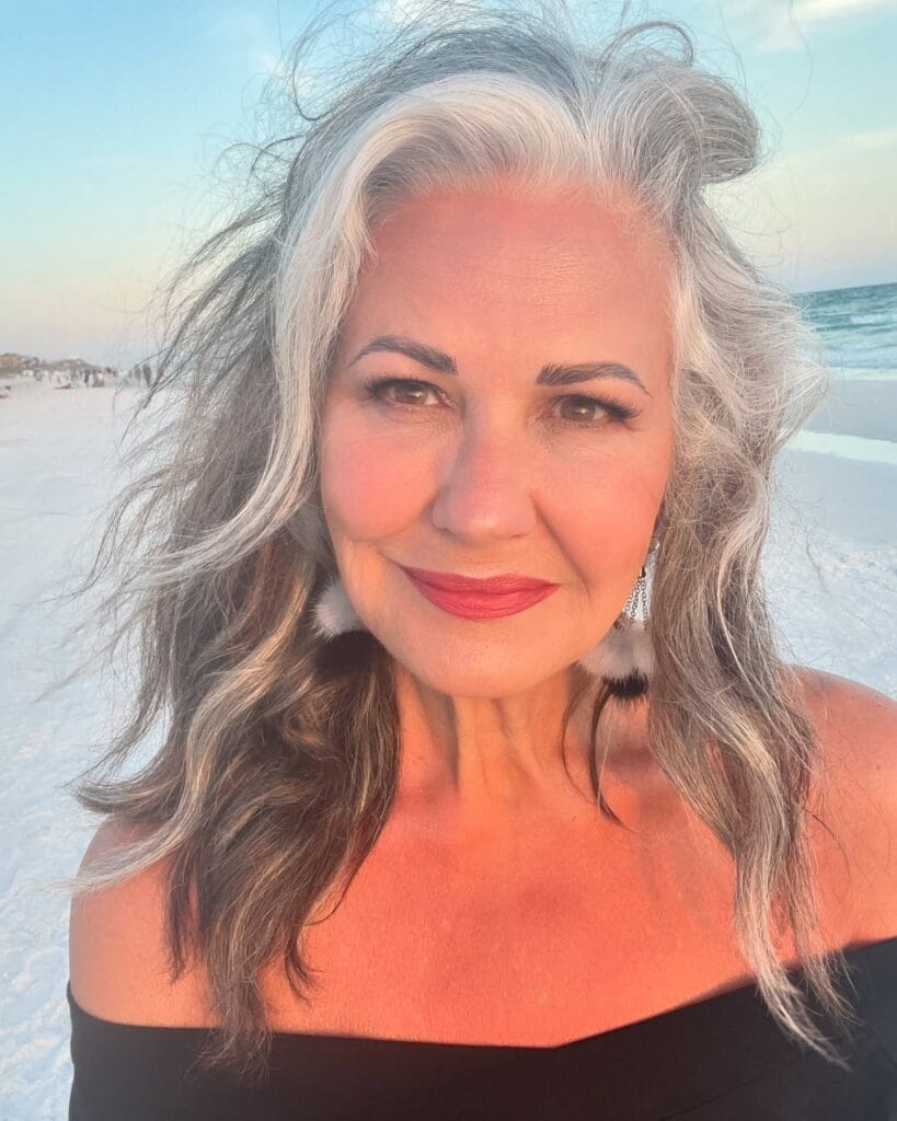 Long wavy gray hairstyle with soft volume and blended tones.