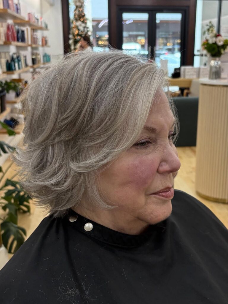 A woman with thick silver hair styled in a feathered collar length bob with voluminous side swept layers.