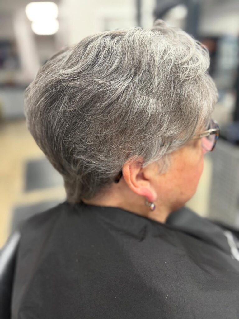 A woman with thick salt and pepper hair showcases a soft tapered pixie cut with voluminous wavy layers on top.