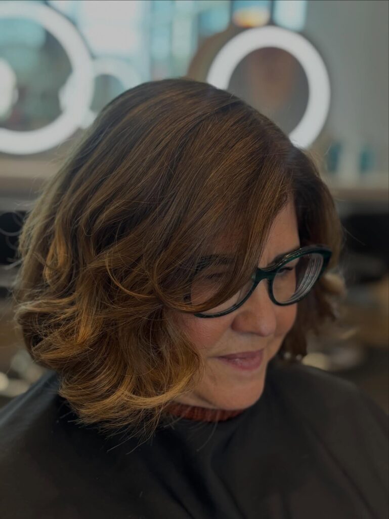 A woman with thick wavy hair in a caramel bronde bob with soft layers and a side part.