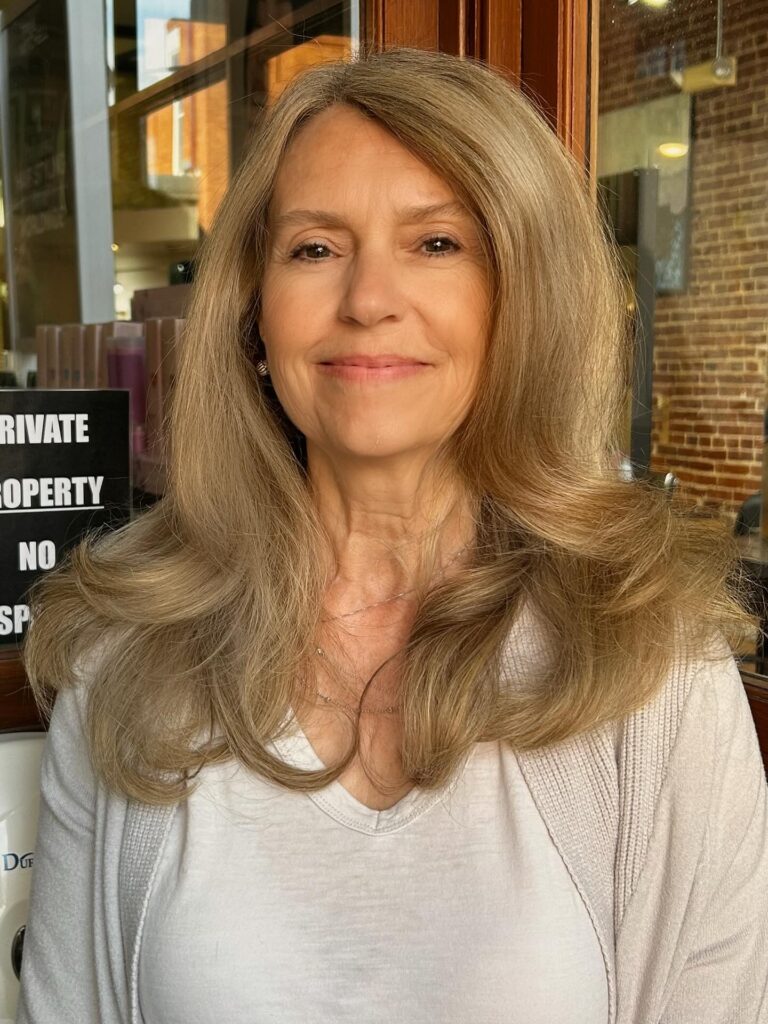 A woman with thick long sandy blonde hair styled in a voluminous blowout with soft outward waves.