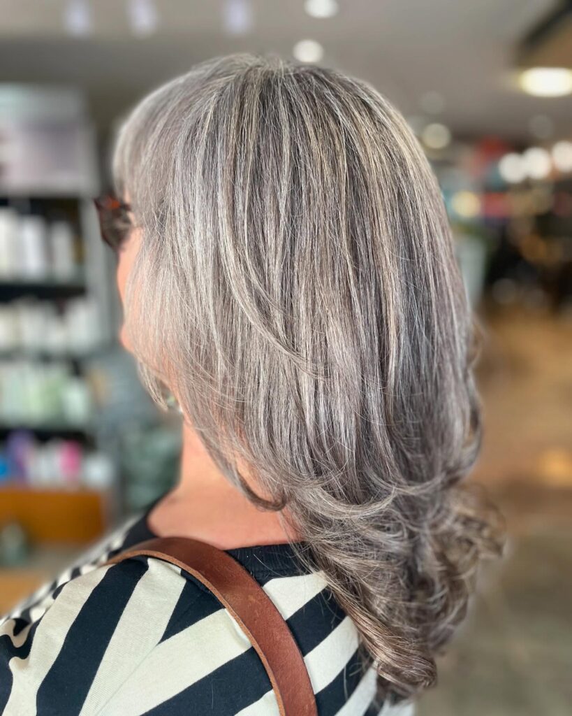 A woman with thick shoulder length silver hair styled with long sweeping layers and soft curled ends.