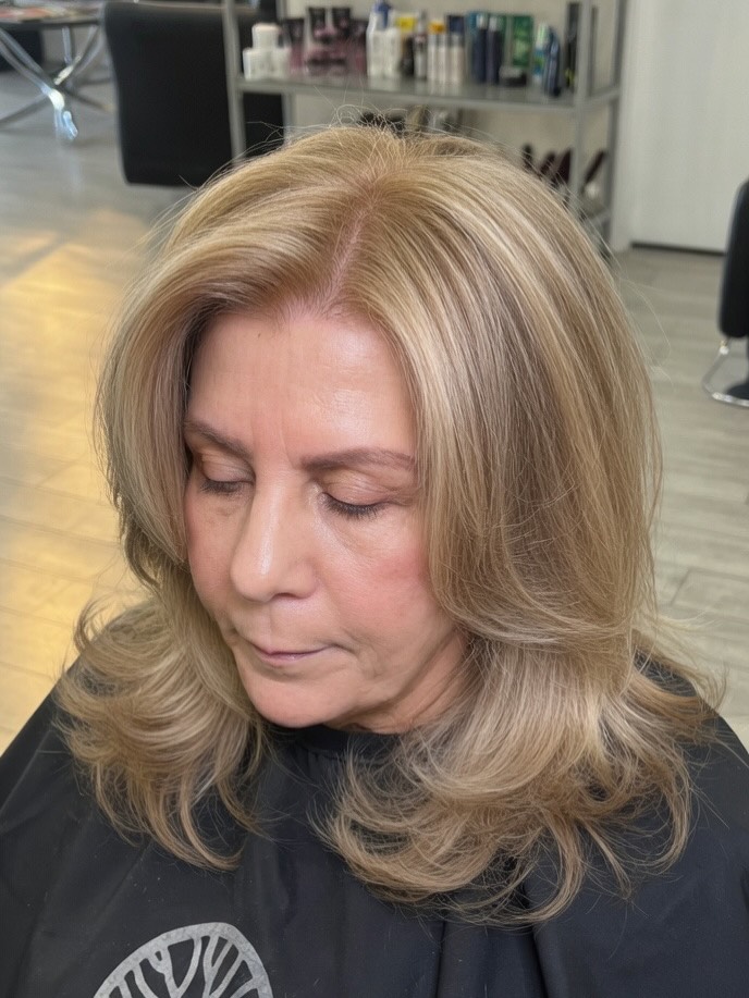 A woman with layered thick honey blonde hair featuring a middle part and curtain bangs styled with bouncy flipped up ends.