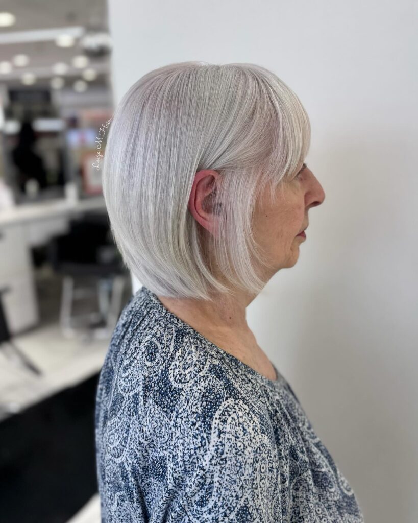 A woman with straight silver hair styled into a sleek chin length bob with soft wispy bangs.