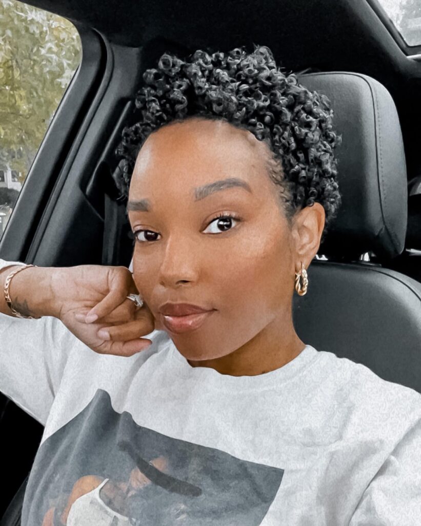 A woman with a short pixie hairstyle featuring glossy defined coily curls and neatly styled edges.
