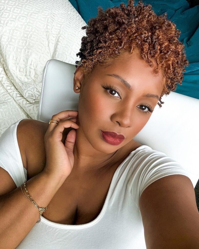A woman with a short honey blonde twist out pixie hairstyle and defined curls.