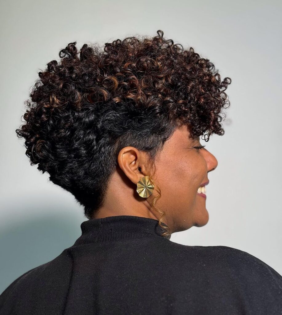 A woman with a curly pixie undercut featuring voluminous curls on top and cropped sides.