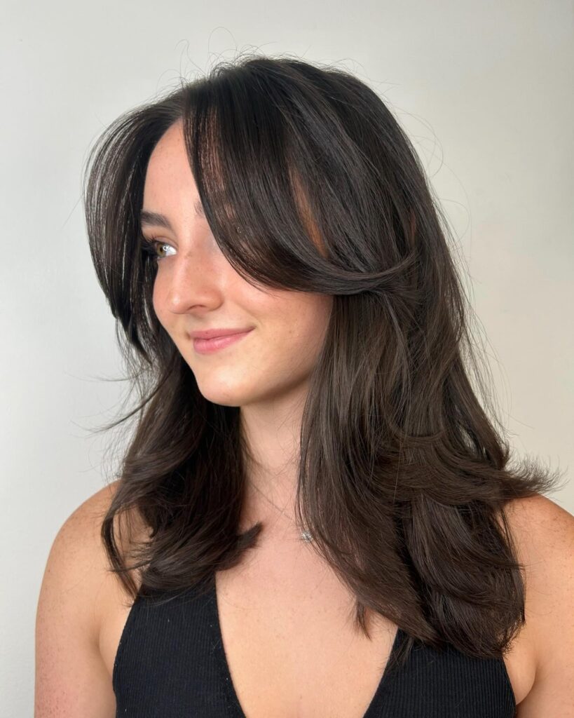 Medium brunette layered hairstyle with curtain bangs and feathered ends.