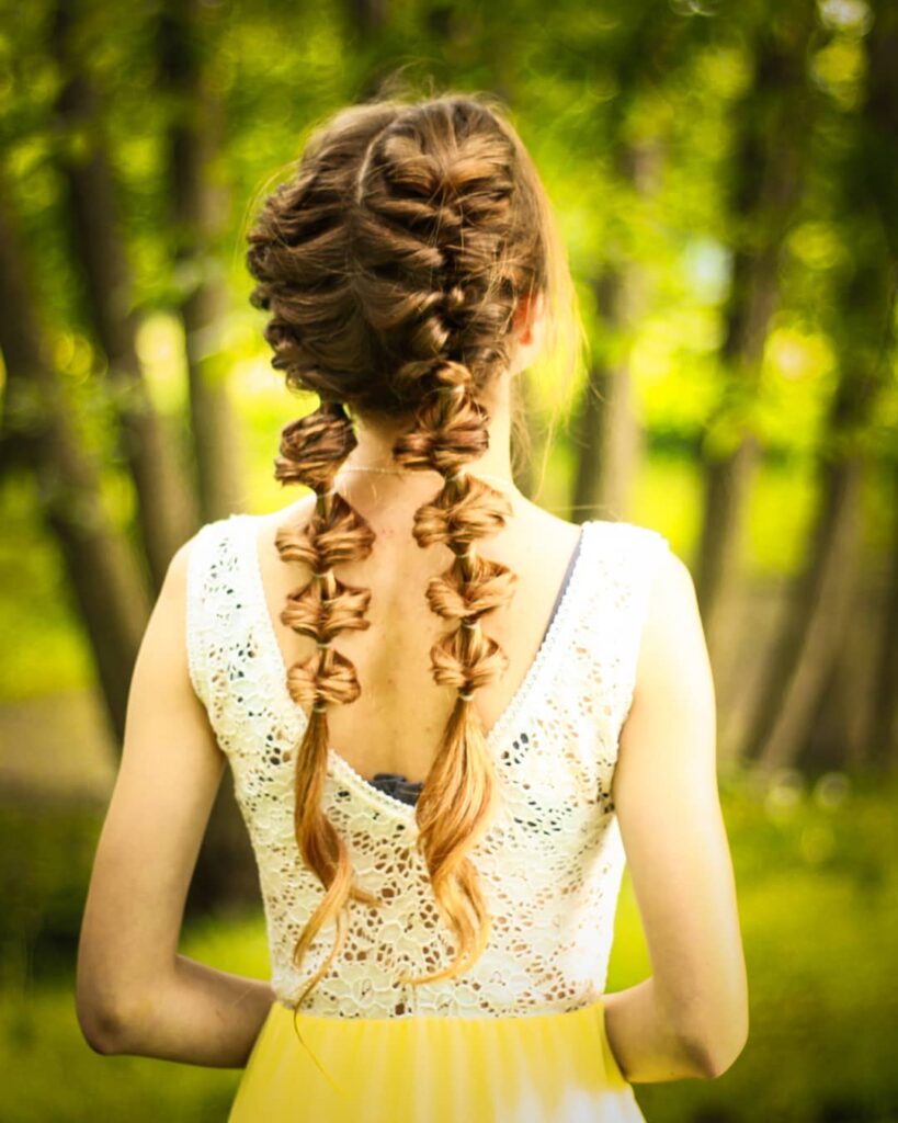 Light brown hair styled in a twisted crown with two long bubble braided pigtails.