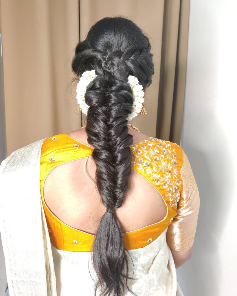 Thick dark fishtail braid with white floral accessories placed on both sides.