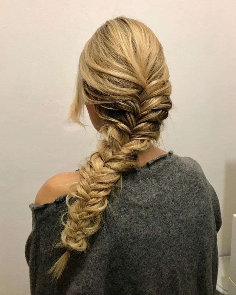 Blonde hair styled in a loose messy side fishtail braid with soft texture.