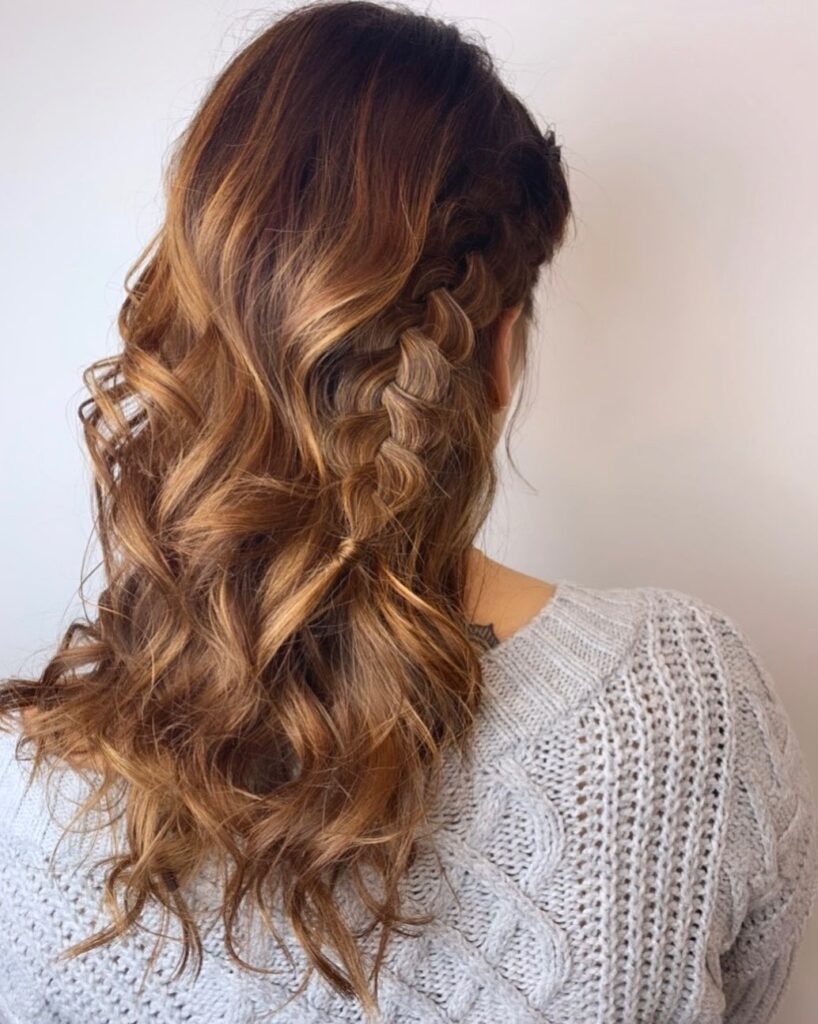 Half up hairstyle with a side braid and loose wavy brown hair.