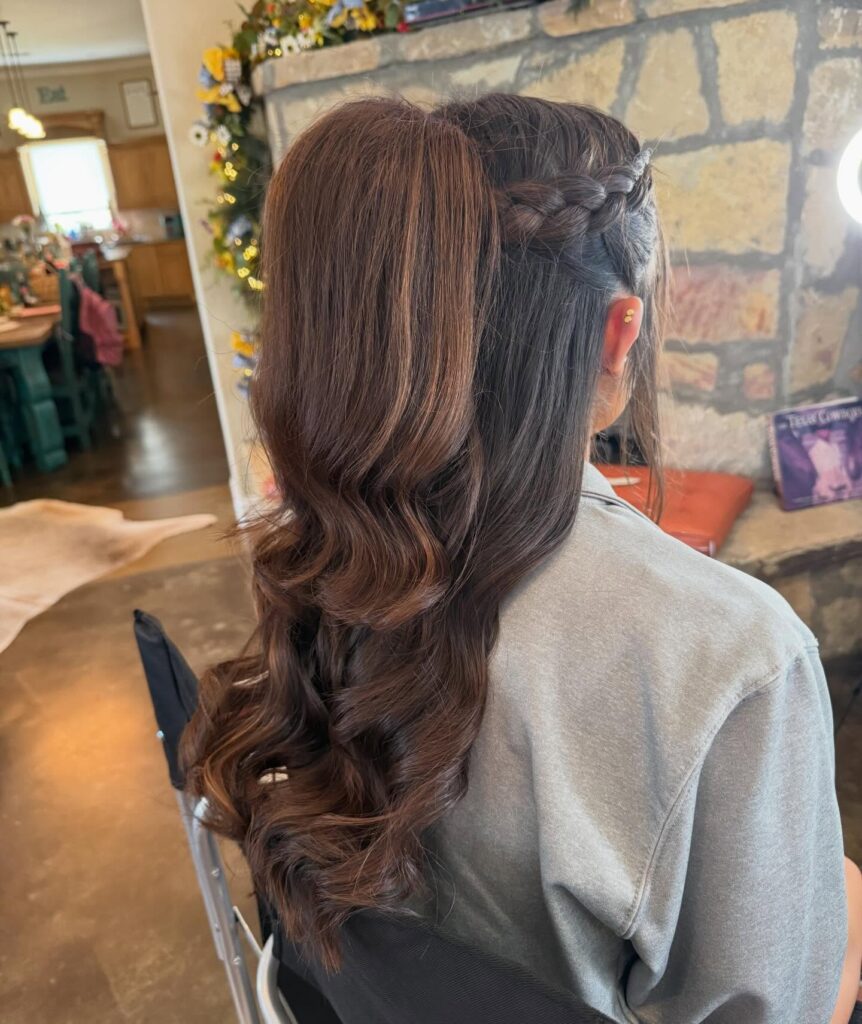 Half up hairstyle with a small side braid and soft curled brunette hair.