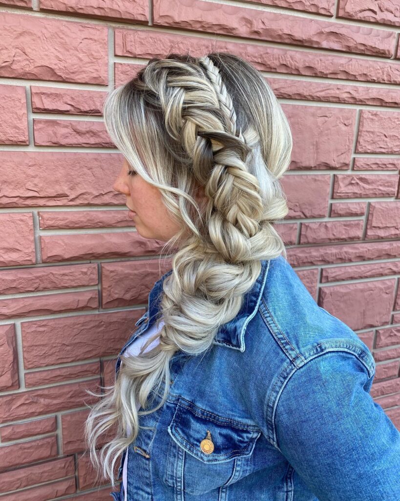 Long blonde hair styled in a voluminous side Dutch braid with loose wavy ends.