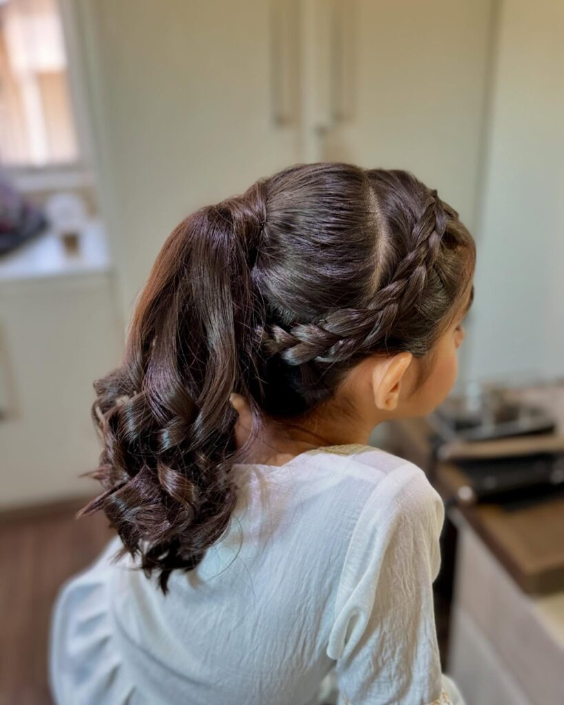 Side braid leading into a low ponytail with curled ends.