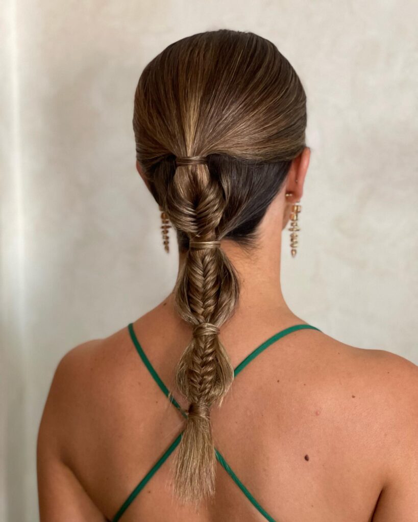 A sleek low bubble braid with small braided sections on dark brown hair.