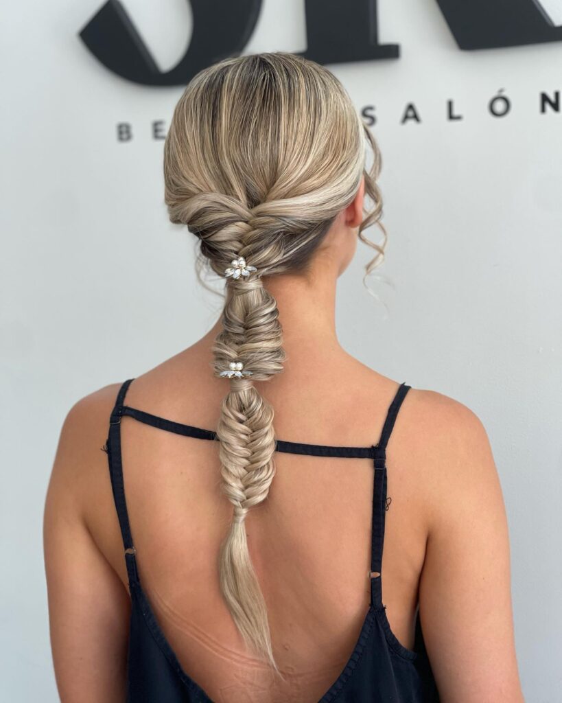 A low bubble braid with a twisted crown detail and decorative accents on blonde hair.