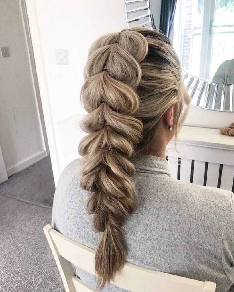 A voluminous blonde bubble braid styled down the back with softly pulled sections for a full look.