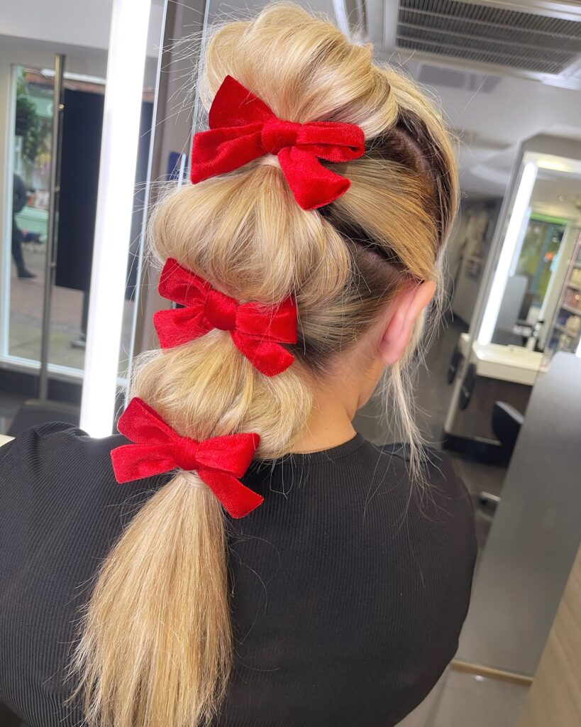 A blonde bubble braid with large red bows placed at each section down the back.