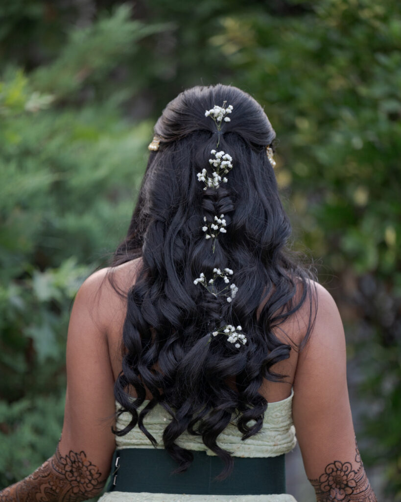 A half up bubble braid with small white flowers placed along dark wavy hair.
