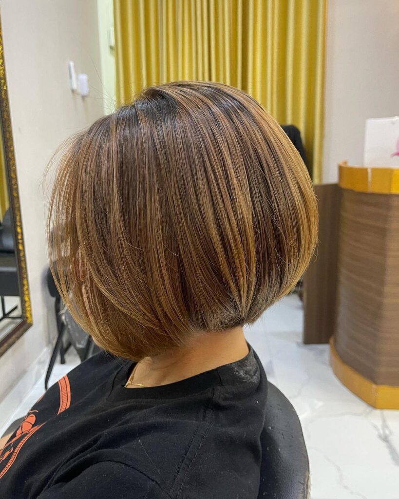 A woman with straight hair is shown from the side wearing a chic angled bob in caramel and honey blonde tones.