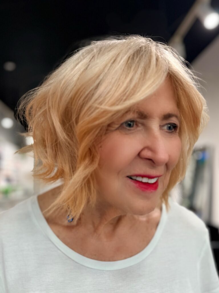 Honey blonde feathered bob with side-swept bangs and softly layered ends.