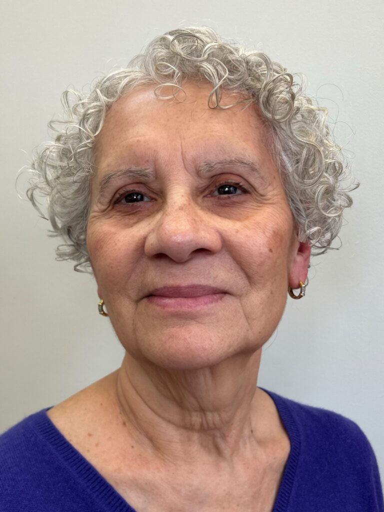 A woman over 60 with short, silver, curly hair styled in a wispy pixie cut that softly frames her face.