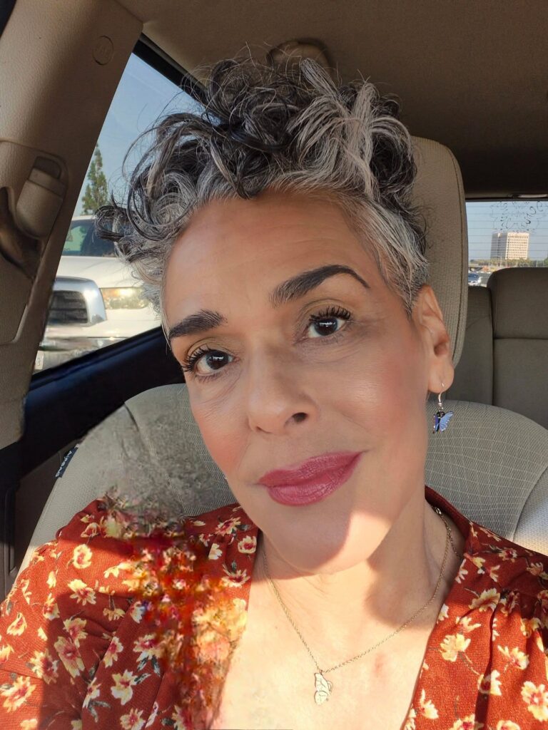 A woman with a short, voluminous pixie cut featuring dark roots and silver curly tips swept upward.