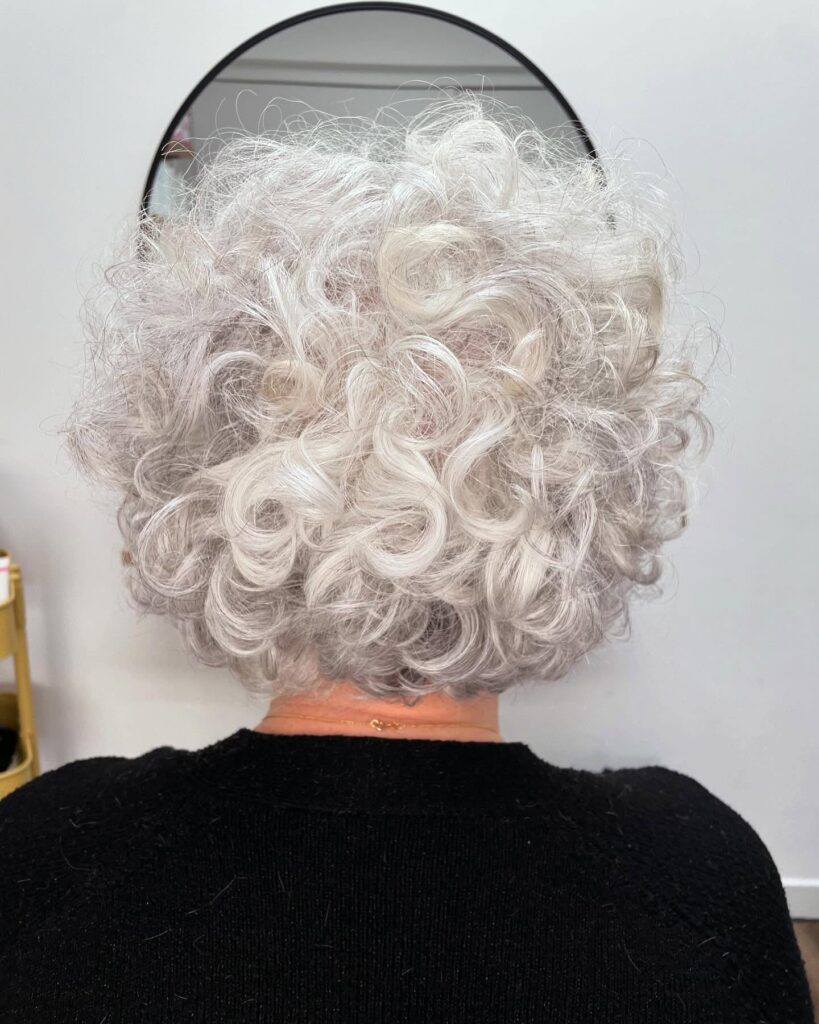 The back view of a woman with a short, rounded bob featuring tight white curls and voluminous spiraled texture.