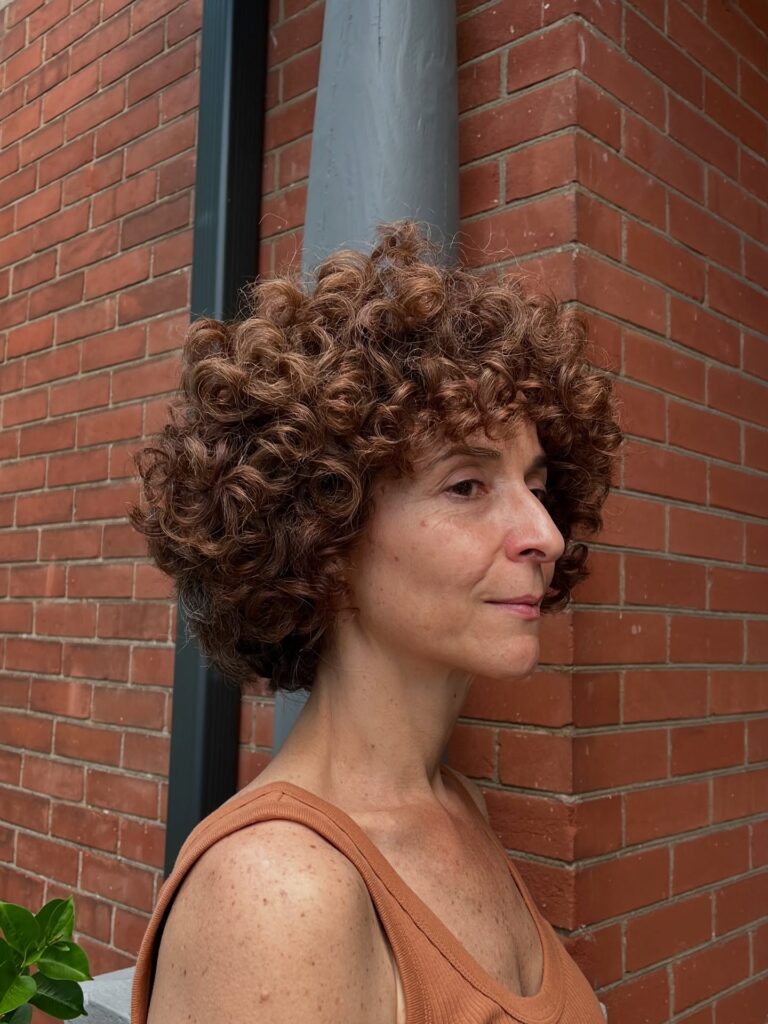 A woman with a short auburn curly shag haircut featuring voluminous corkscrew ringlets and a curly fringe.