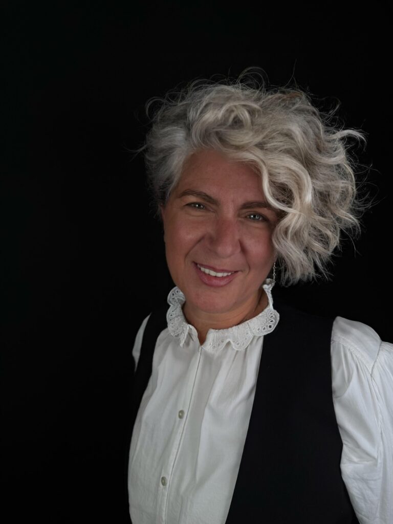 A woman with a short asymmetrical silver hairstyle featuring a long side-swept wavy fringe and voluminous platinum curls.