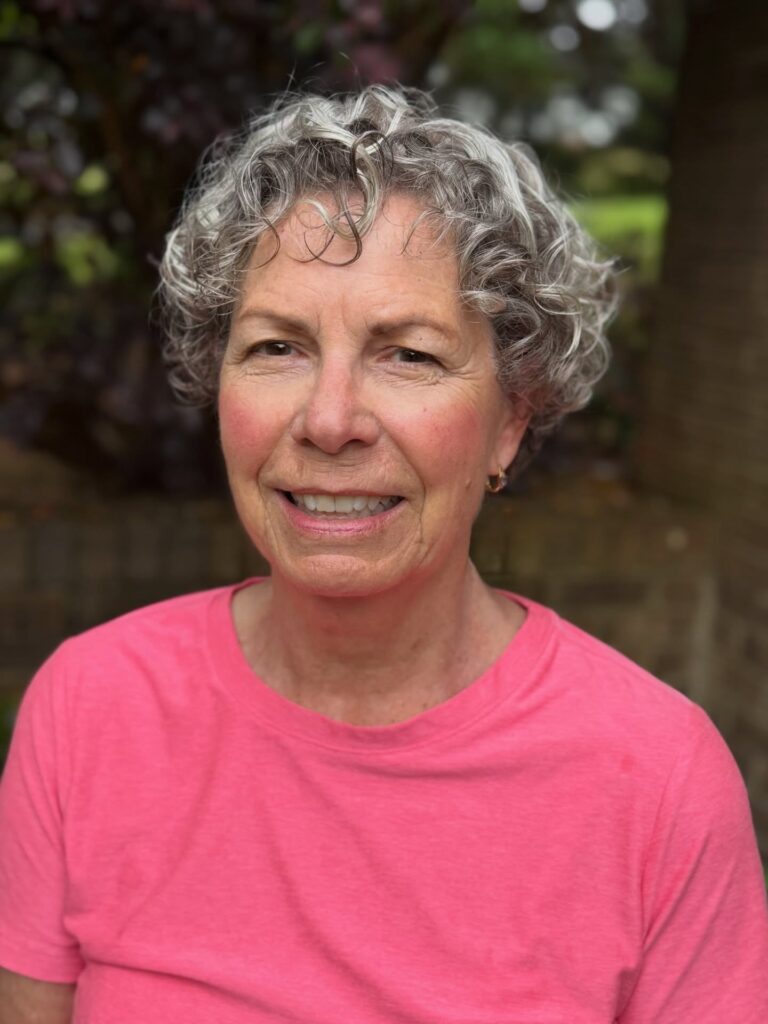 An older woman with an ear-length salt-and-pepper curly hairstyle featuring loose grey ringlets and a soft side part.