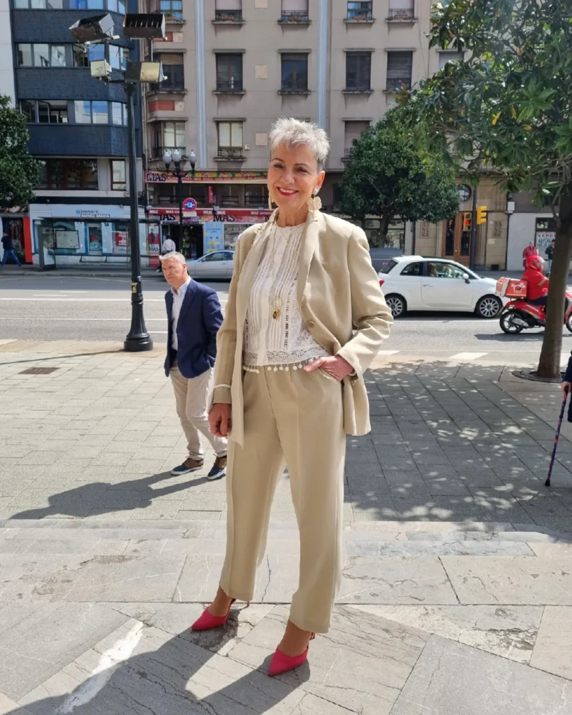 A woman standing outdoors with a short spiky tapered pixie cut in a natural salt and pepper grey color.