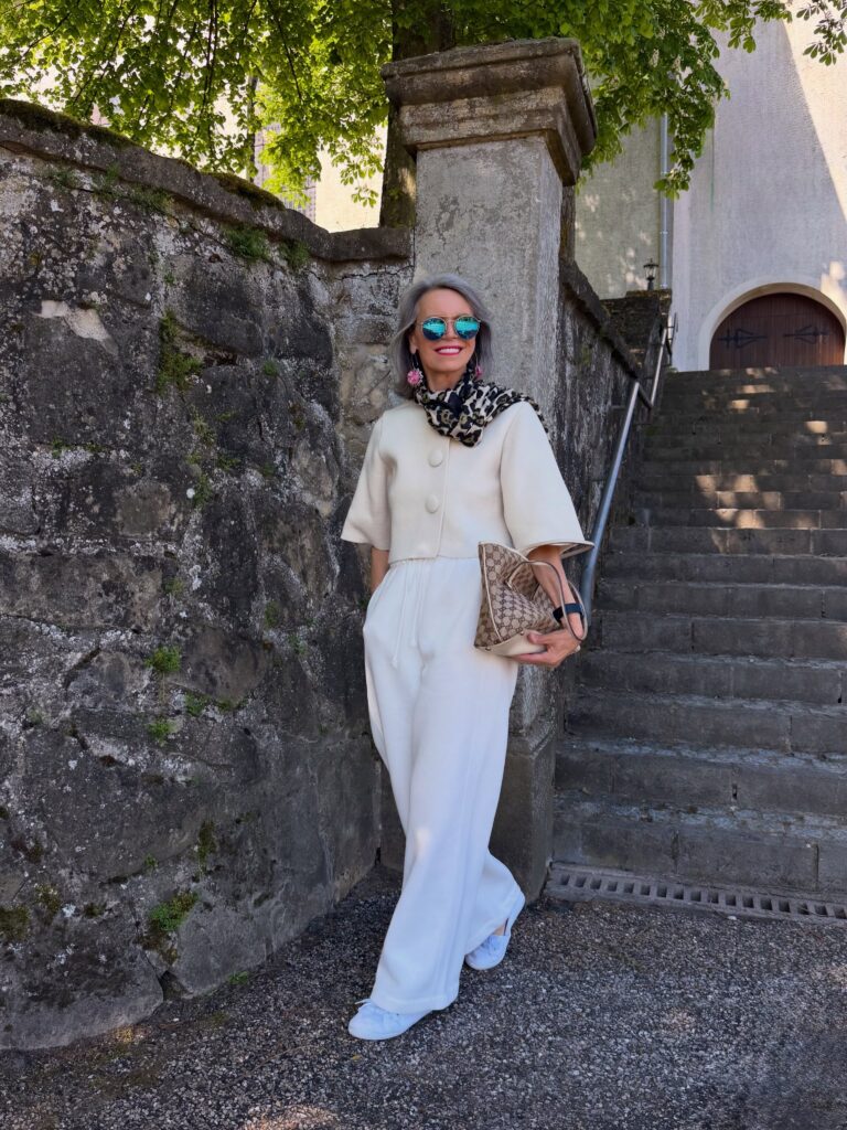 A woman standing outdoors wearing blue mirrored sunglasses and a sleek shoulder length grey lob with a side part.