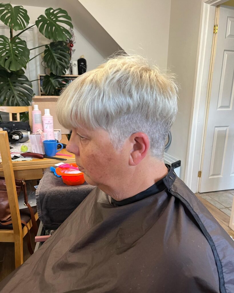 A woman with a bright silver pixie cut featuring a longer textured top and a closely cropped undercut.