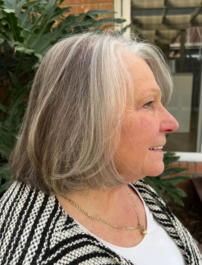 A woman over 60 with a chin length salt and pepper bob featuring soft layers and silver face framing highlights.