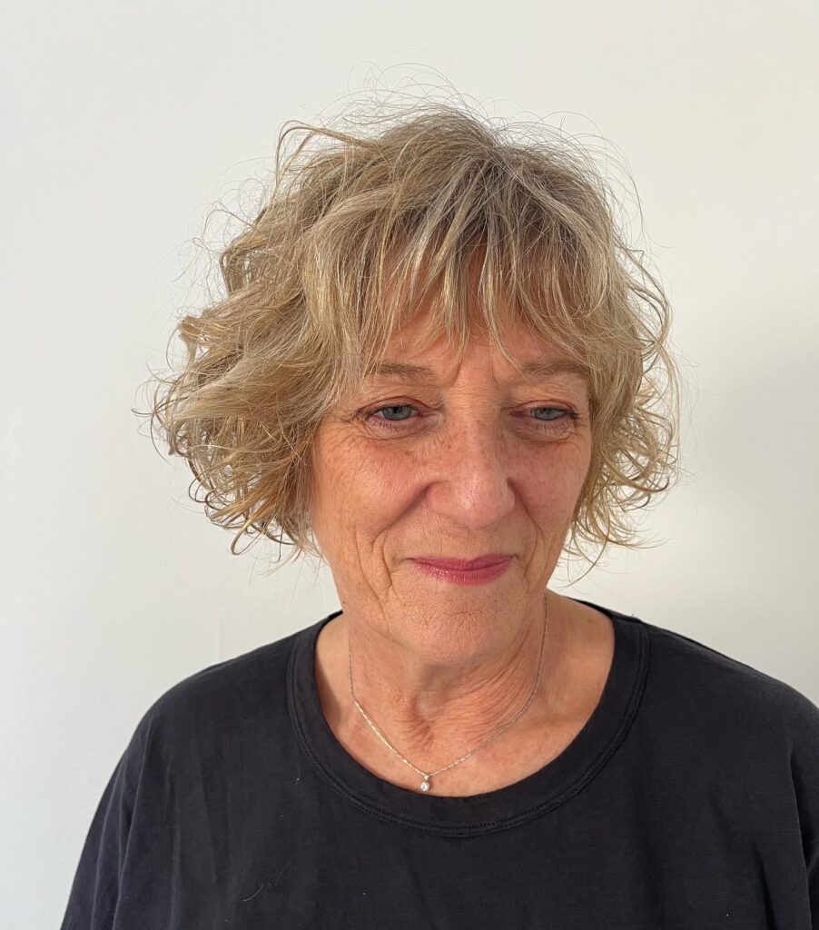 A woman with a chin-length curly blonde bob and light wispy bangs.