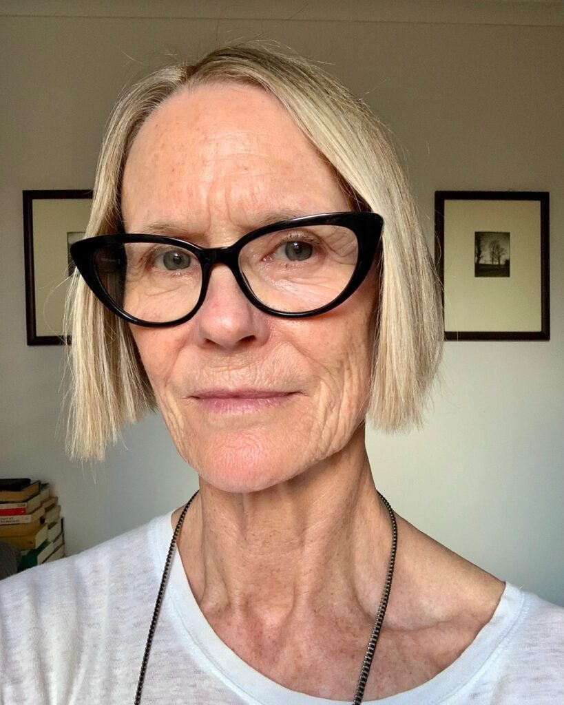 A woman wearing cat-eye glasses with a sharp, chin-length blunt blonde bob.