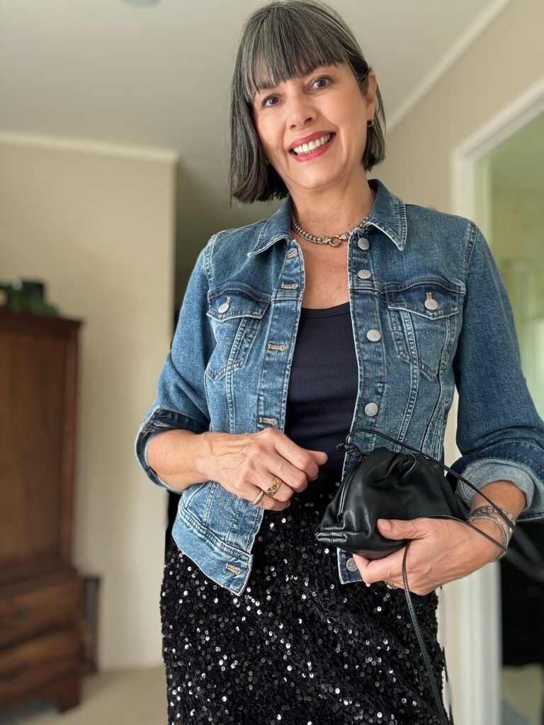 A smiling woman with a chin-length salt and pepper bob and straight bangs wearing a denim jacket.