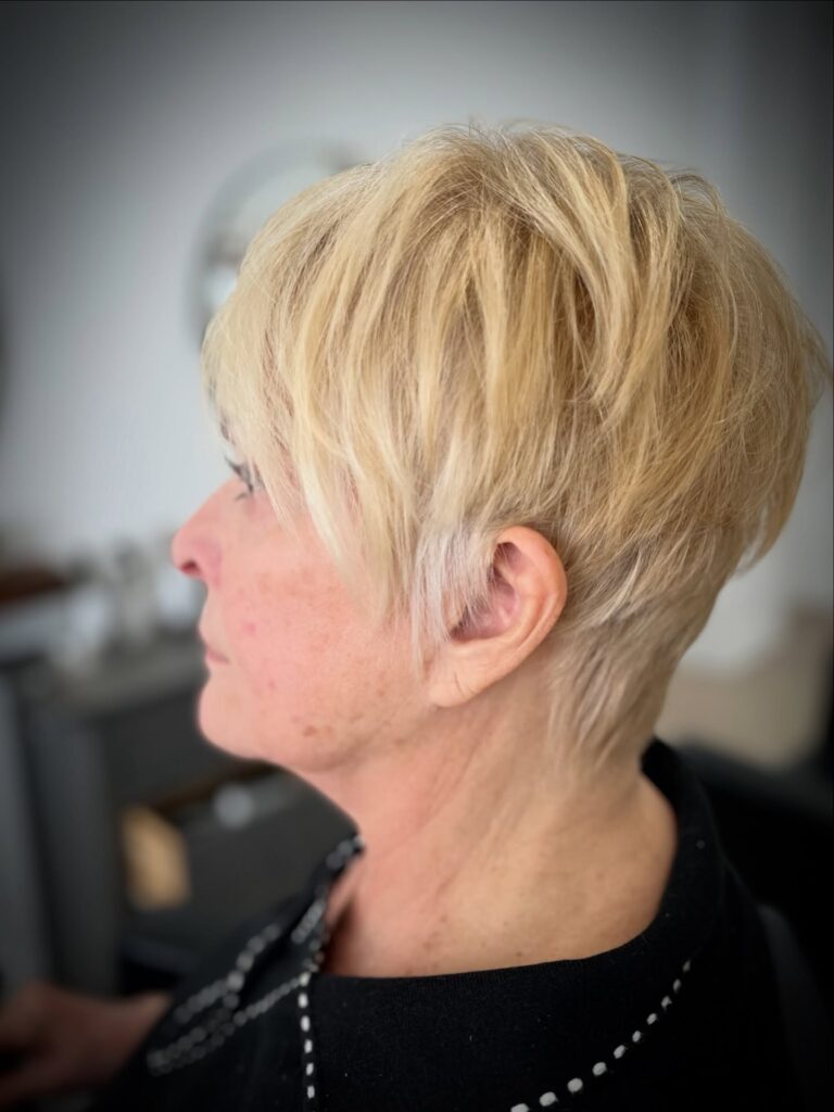 A side profile view of a woman over sixty with a bright golden-blonde wispy pixie haircut.